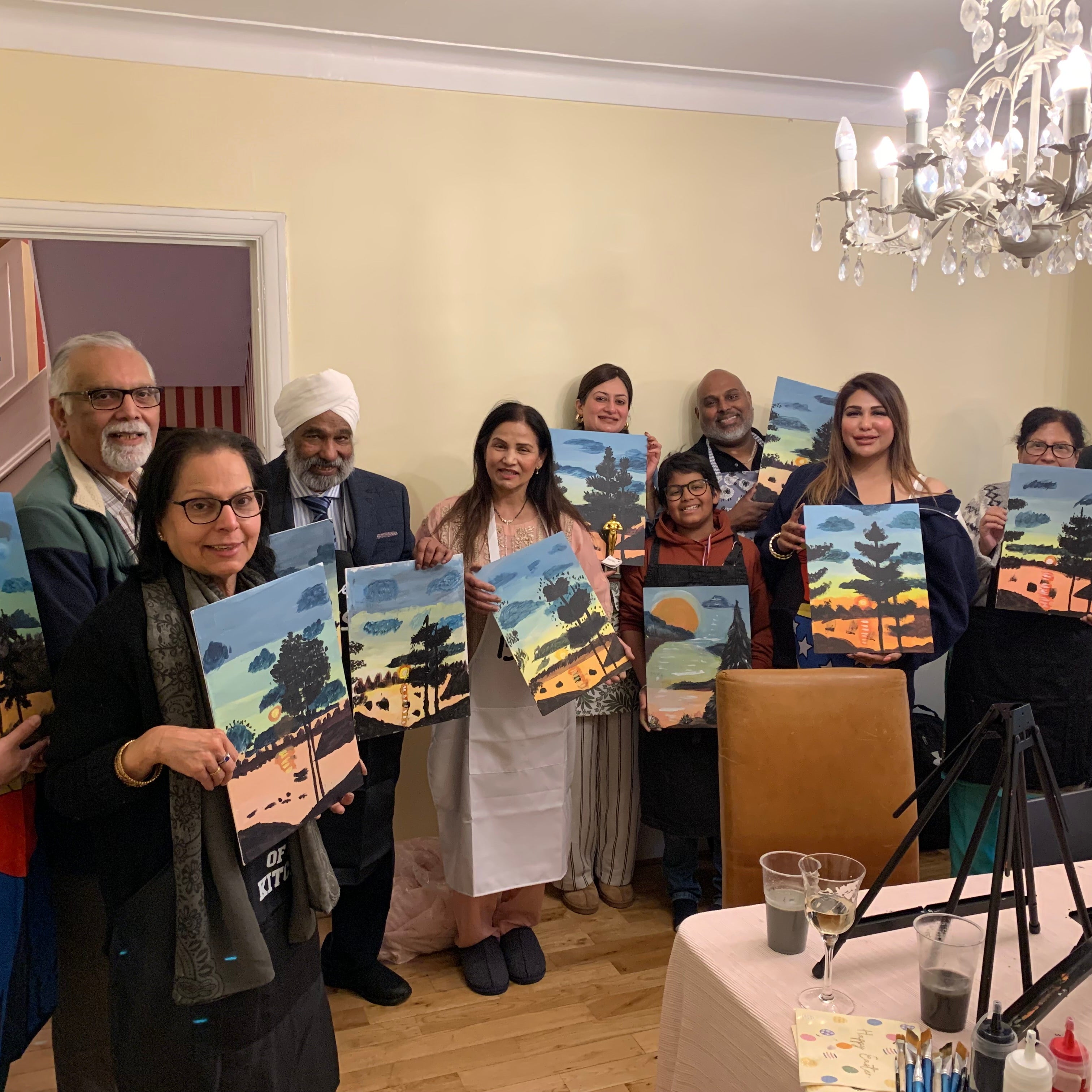 Group of people holding artworks in a room with a chandelier.